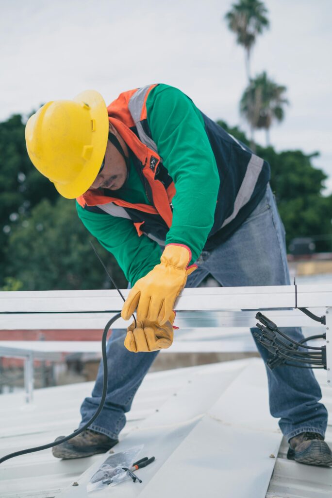 pexels photo 8853472 8853472 A construction worker wearing PPE installs electrical equipment on a roof.